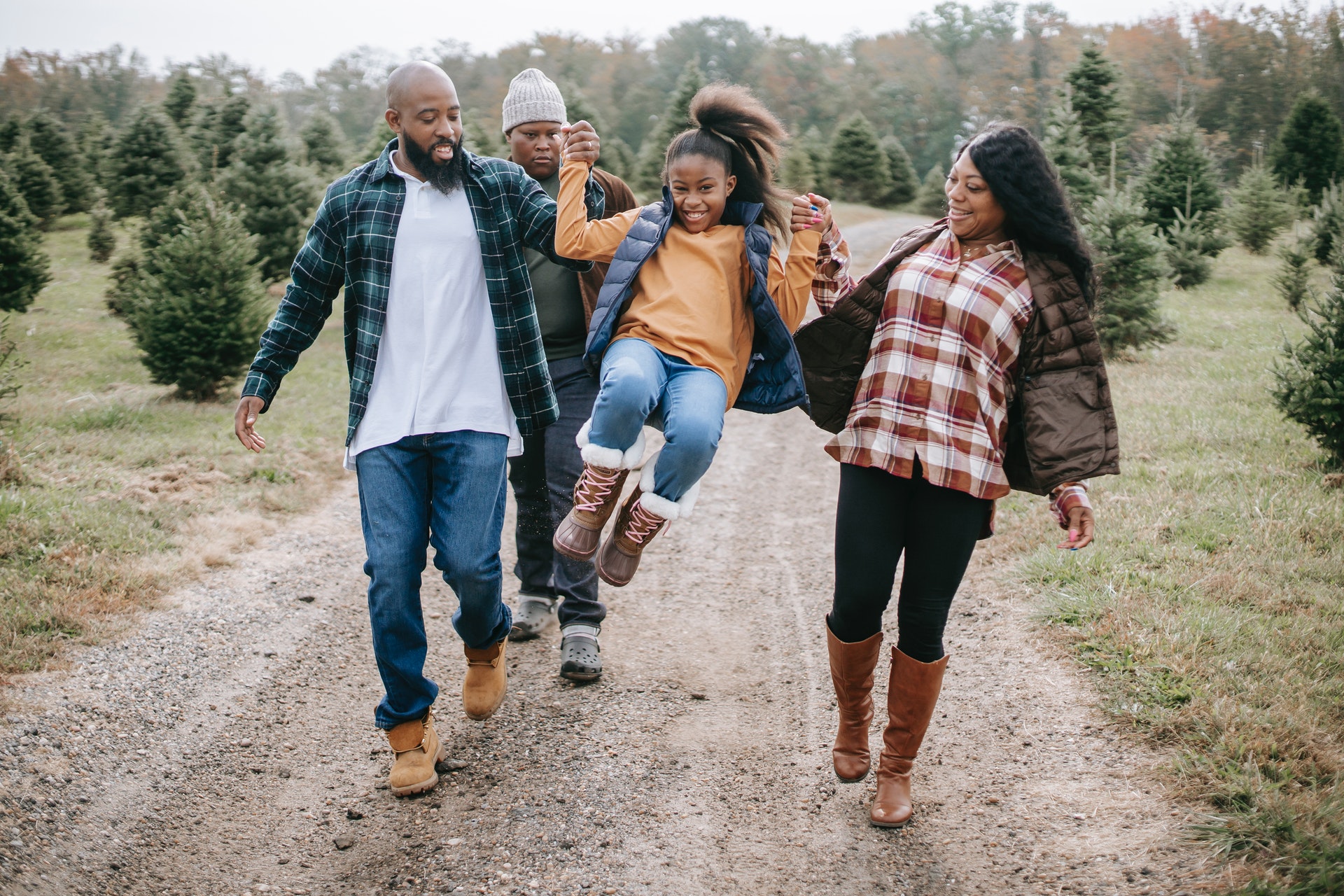 Black family with daughter swinging between the two of them in a christmas tree lot